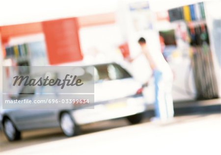 Person filling up car at gas station, blurred