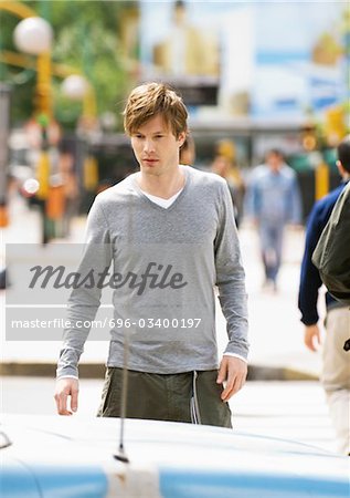 Young man crossing street, looking down at car