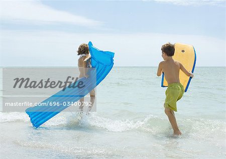 Children running in surf at beach, with raft and body board