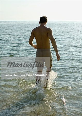 Man splashing in surf, rear view