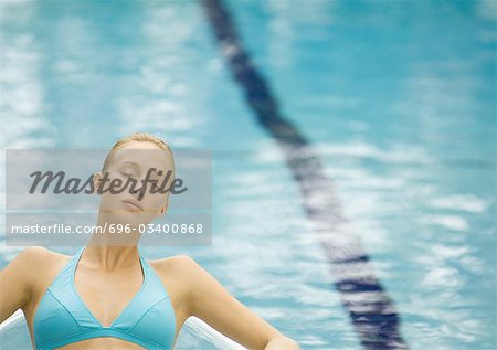 Femme reposante près de la piscine avec les yeux fermés