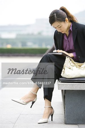 Jeune femme d'affaires assis sur un banc, regardant vers le bas de téléphone portable