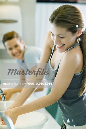 Two women washing hands in sinks, one getting splashed