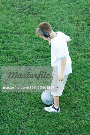 Boy standing with ball, wearing headphones