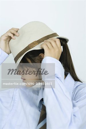 Teenage girl wearing shirt and tie, pulling hat down over eyes, portrait