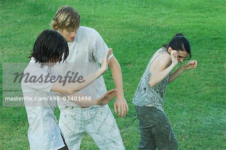 Group of young friends standing in water spray, getting wet