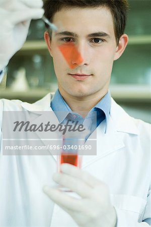 Young male lab worker holding up microscope slide and beaker