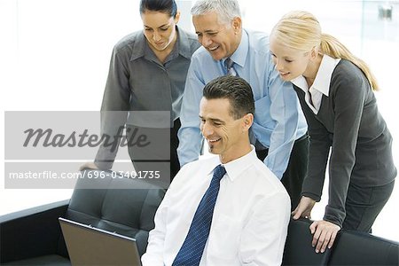 Businessman using laptop while colleagues look over shoulder