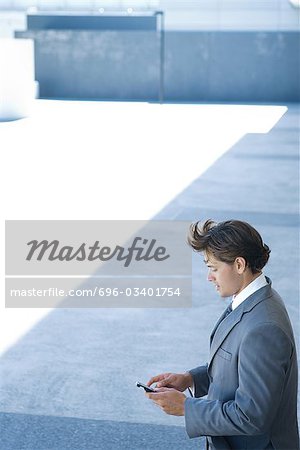Homme d'affaires permanent à l'extérieur, regardant vers le bas au téléphone cellulaire, vue grand angle