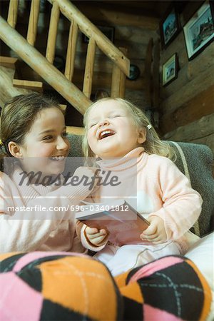 Mädchen und Kleinkind auf Couch sitzen, lachen