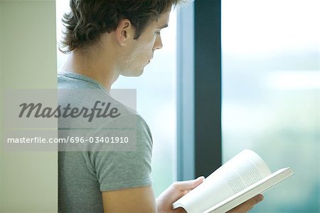 Young man reading book by window, side view