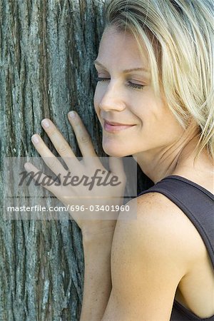 Woman leaning against tree trunk, eyes closed, smiling, cropped view, full frame
