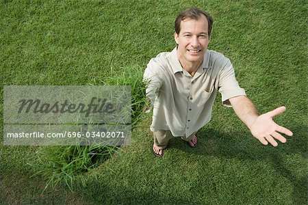 Man standing and holding clump of grass in one hand, smiling at camera, high angle view