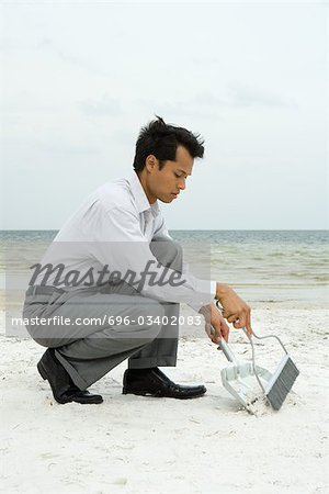Man crouching on beach using broom and dustpan