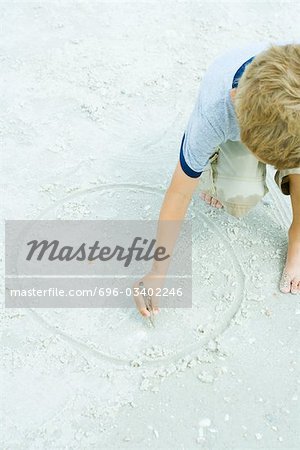 Child drawing circle in the sand with a stick, cropped view