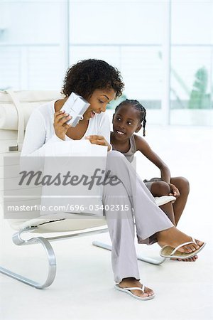 Mother sitting next to daughter, holding up gift, both smiling