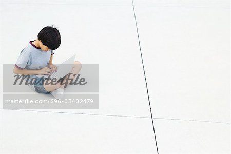 Boy sitting cross-legged on the ground, using laptop, high angle view