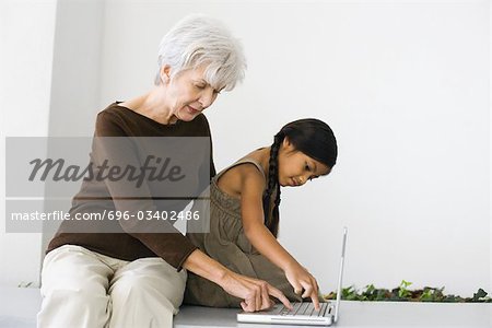 Senior Woman sitting hinter Enkelin, tippen auf Laptop zusammen