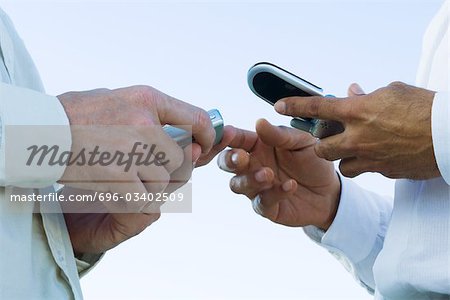 Deux hommes face à face, tenant des téléphones cellulaires, recadrée affichage des mains