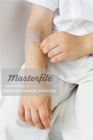Little boy picking at adhesive bandage on his arm, cropped view