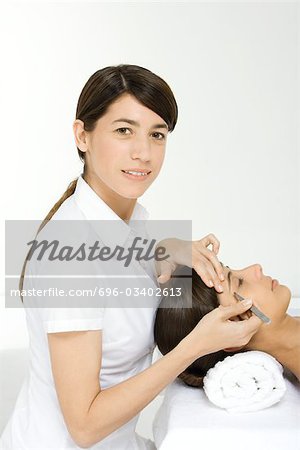 Beautician smiling at camera and plucking a woman's eyebrows