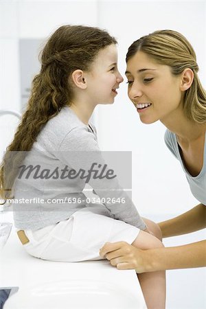 Little girl whispering in her mother's ear, side view