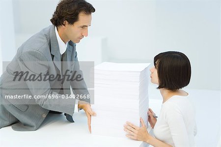 Boss pushing stack of paper across desk to his assistant