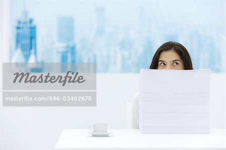 Woman sitting behind stack of paper, looking over and away