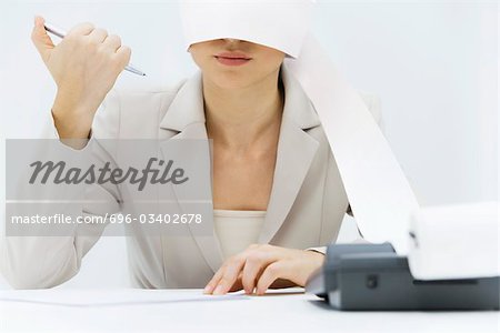 Woman sitting at desk with adding machine tape wrapped around her head, clicking pen