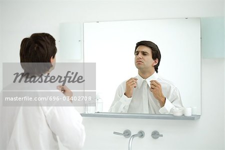 Man wearing button down shirt, adjusting collar in mirror