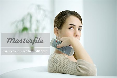Femme tenant la télécommande, regarder par-dessus l'épaule à la caméra