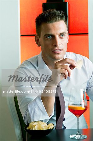 Jeune homme assis avec un verre de vin orange et pommes frites
