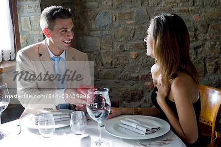 Young man giving a present to young woman at restaurant table