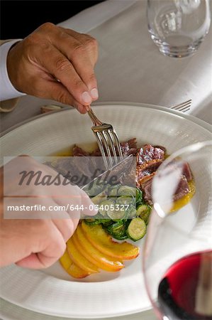 Gros plan des mains du jeune homme avec un couteau et une fourchette dans son assiette