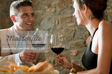 Couple sitting at restaurant table toasting with red wine