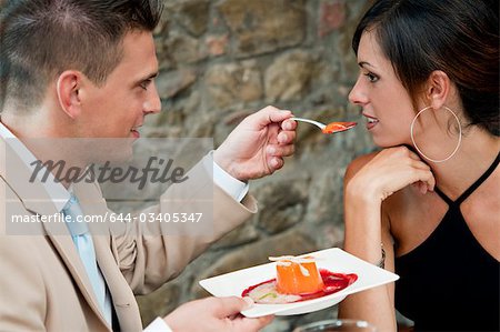 Young man feeding young woman at restaurant