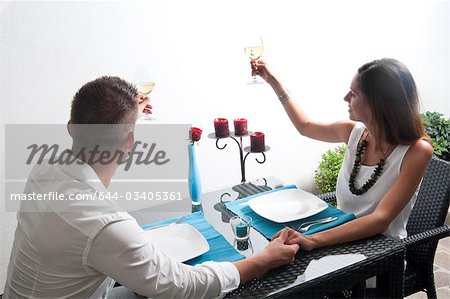 Paar, sitzen am Tisch Toasten mit Weißwein und Hand in Hand