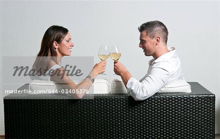 View of couple from the back sitting on couch toasting with white wine