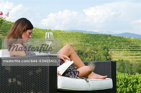 Jeune femme assise sur le canapé dans la vigne au vin blanc, lire un livre