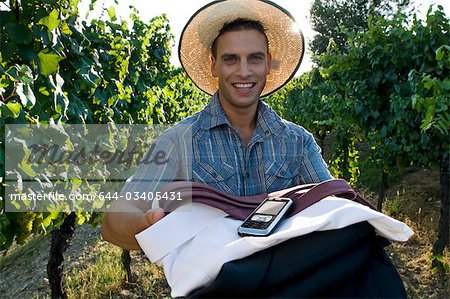 Jeune homme en tenue décontractée avec des vêtements de travail pliés et téléphone mobile