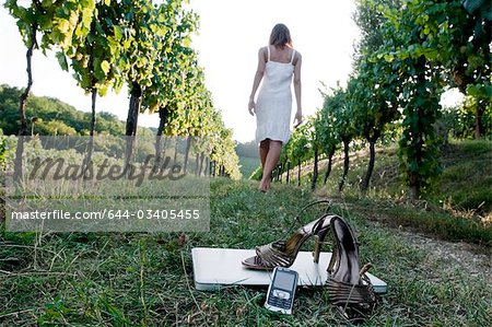 Young woman  in vineyard with high heel shoes, mobile, and laptop in foreground