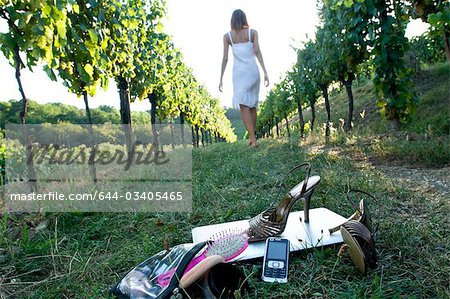 Junge Frau im Weinberg mit high heels Schuhe, Handy, Laptop und Körperpflege Tasche im Vordergrund