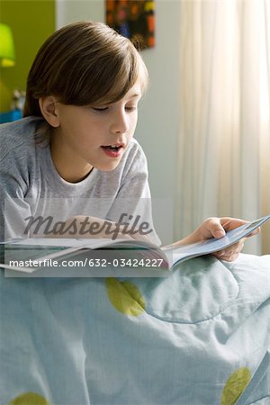 Boy lying on bed reading book