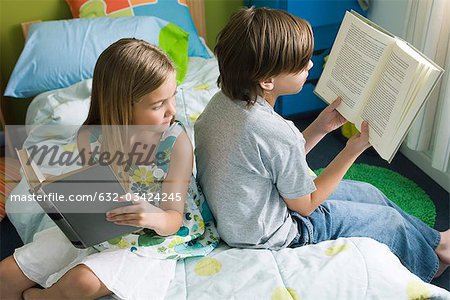 Siblings reading together, girl glancing over shoulder at brother's book