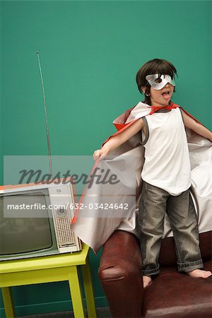 Boy in superhero costume standing on sofa