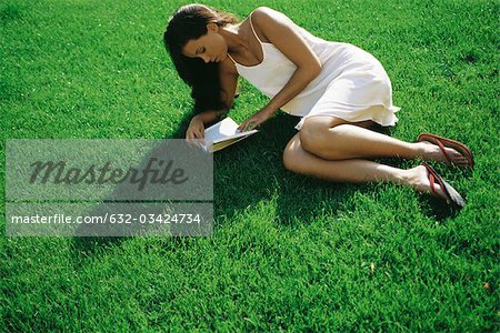 Young woman lying on grass reading book