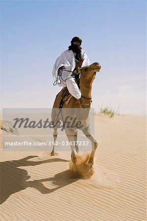 Mali, Timbuktu. Dans le désert au nord de Timbuktu, un homme touareg chevauche son chameau sur une dune de sable. Il oriente l'animal avec ses pieds.