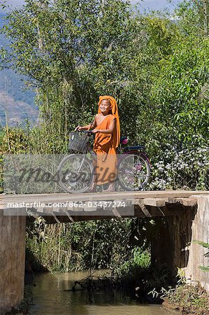 Myanmar, Burma, Pan-lo. Ein stolzer junger Novize überquert eine Holzbrücke mit seinem Fahrrad in der Nähe von Pan-lo-Dorf. Die Räder des Motorrades sind dekoriert mit CDs.