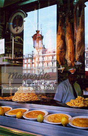 Hams hang above a food counter in the window of a restaurant in the Plaza Major