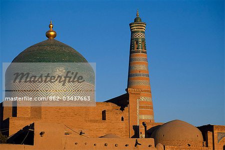 The minaret and tiled dome of a mosque rise above the old city of Khiva. The dome is covered in Khiva's hallmark green ceramic tiles.